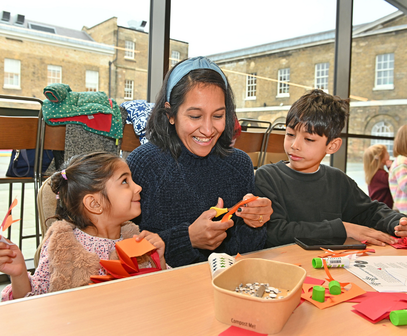 A woman cutting paper during a crafternoon at Woolwich Works while two children look on