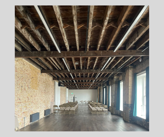 Inside Beanfeast, a medium-sized space at Woolwich Works, with exposed wooden roof beams, with chairs set up and light coming in through the windows