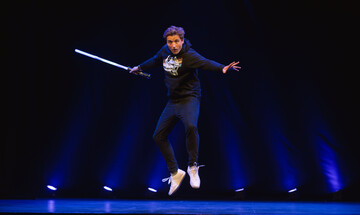 Comedian Jon Hipkiss leaping in the air wearing a Star Wars t-shirt and holding a light sabre.