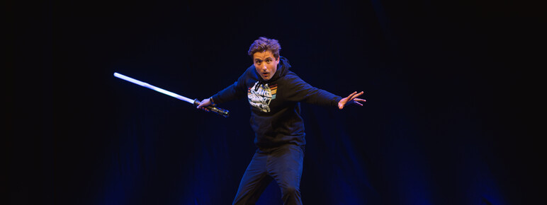Comedian Jon Hipkiss leaping in the air wearing a Star Wars t-shirt and holding a light sabre.