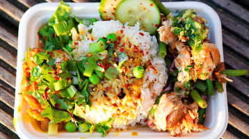 A takeaway tray of well dressed prawns, rice and vegetables