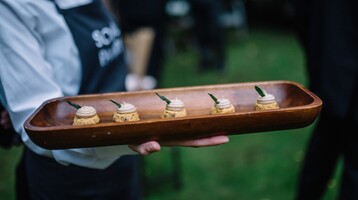 A wooden tray of gourmet canapes are held by a server wearing a Social Pantry apron